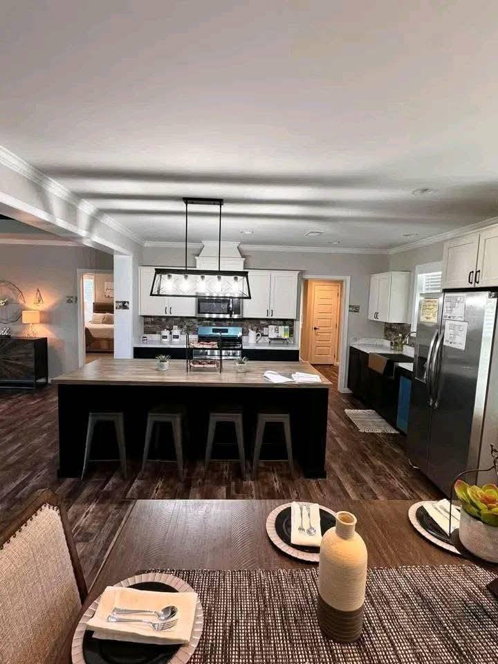 Spacious kitchen with dark wood flooring, large island with stools, modern appliances, and elegant lighting. Cozy, inviting atmosphere.