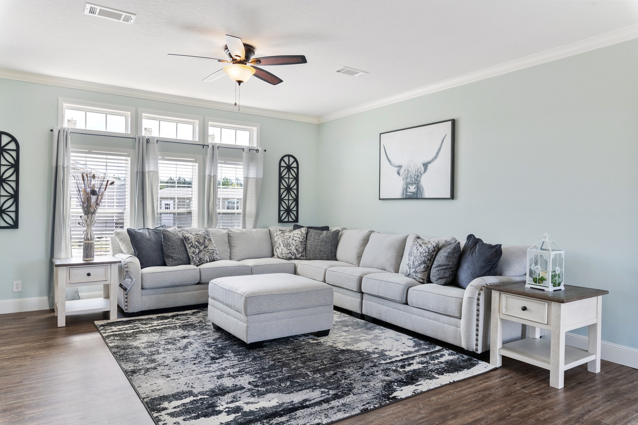 Spacious living room with a gray sectional sofa, patterned cushions, and a matching ottoman. Art features a bull, enhancing the serene, modern decor.
