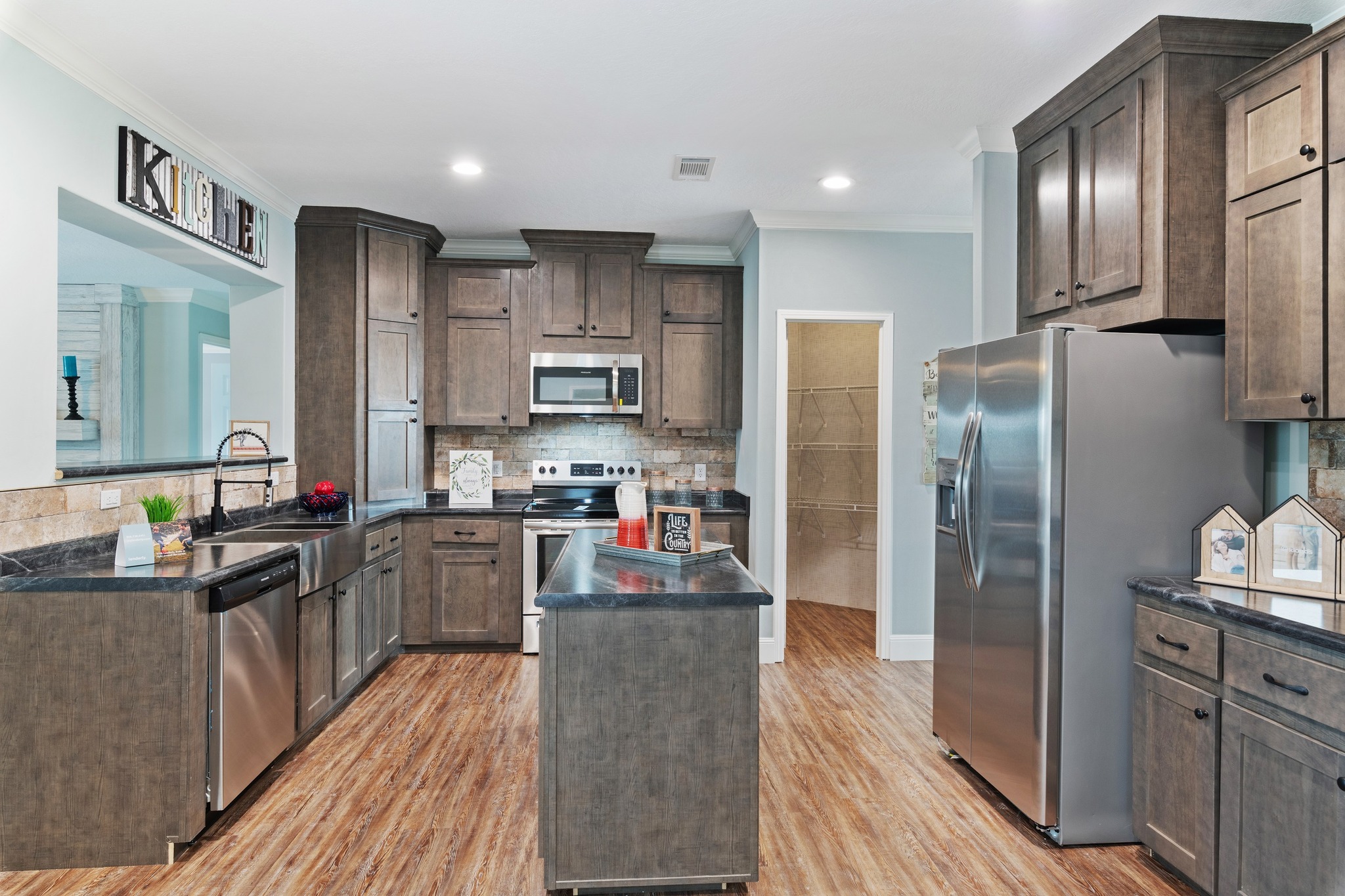 Spacious kitchen with wooden cabinets, stainless steel appliances, and a central island. Warm lighting and wood flooring create a cozy atmosphere.
