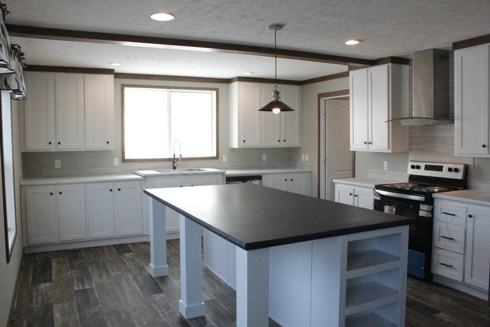 Spacious kitchen with a central black island, white cabinets, dark wood floors, and stainless-steel appliances. Bright window light and modern finish.