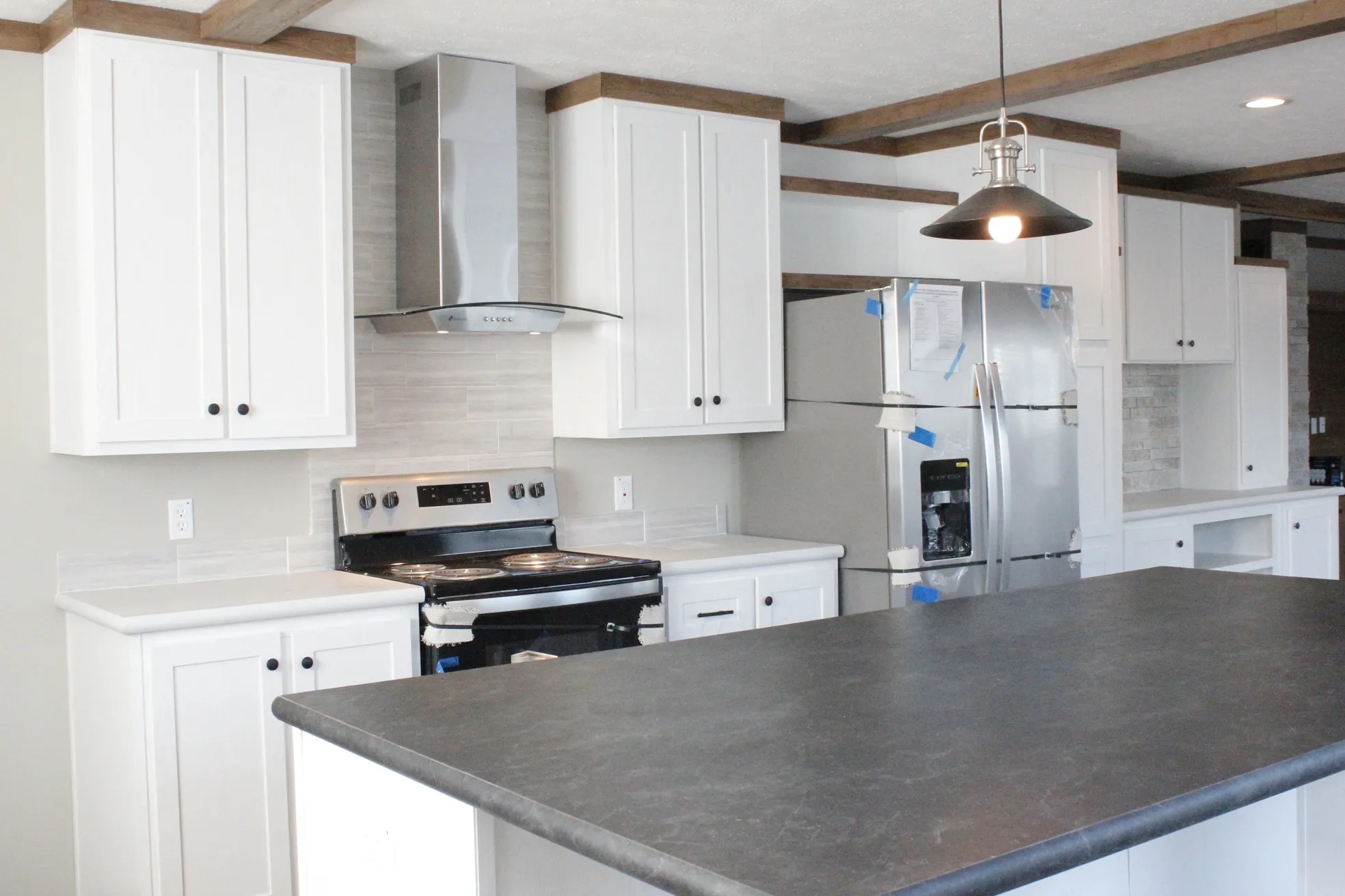 Modern kitchen with white cabinets, stainless steel appliances, and a sleek gray countertop island. The space is bright and contemporary with a warm tone.