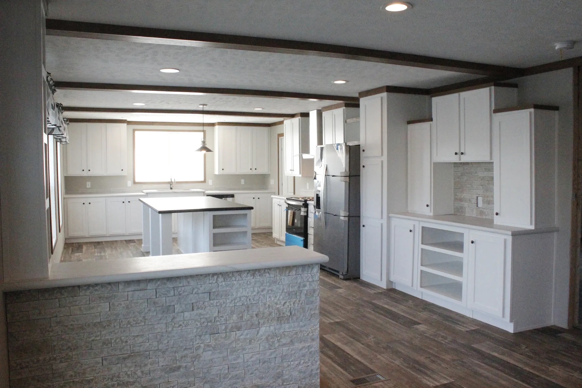 Spacious modern kitchen with white cabinets, stainless steel appliances, and a central island. Wooden floor and subtle lighting create a warm ambiance.