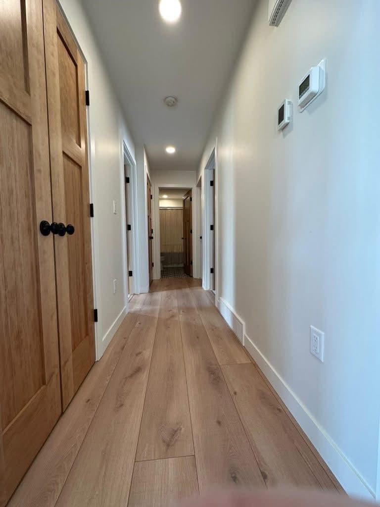 Wooden floor hallway with white walls, two wooden doors on the left, and three doors on the right. Bright lighting creates a warm, inviting atmosphere.