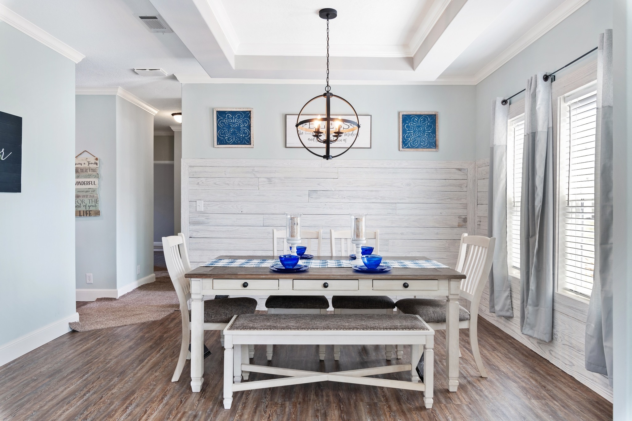 Bright dining room with white table and chairs, blue accents, and a modern chandelier. Rustic wood floors and walls create a cozy, inviting atmosphere.