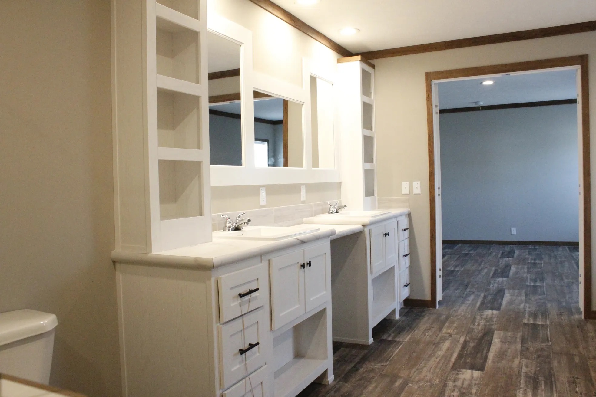 Spacious bathroom with dual sinks on a long white vanity featuring open shelves and mirrors. Warm lighting and wood-style tile flooring add elegance.