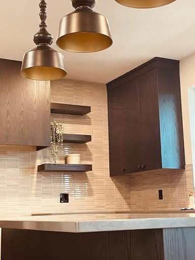 Modern kitchen with dark wood cabinets, open shelves with decor, and metallic pendant lights. Neutral tile backsplash adds a warm, inviting tone.