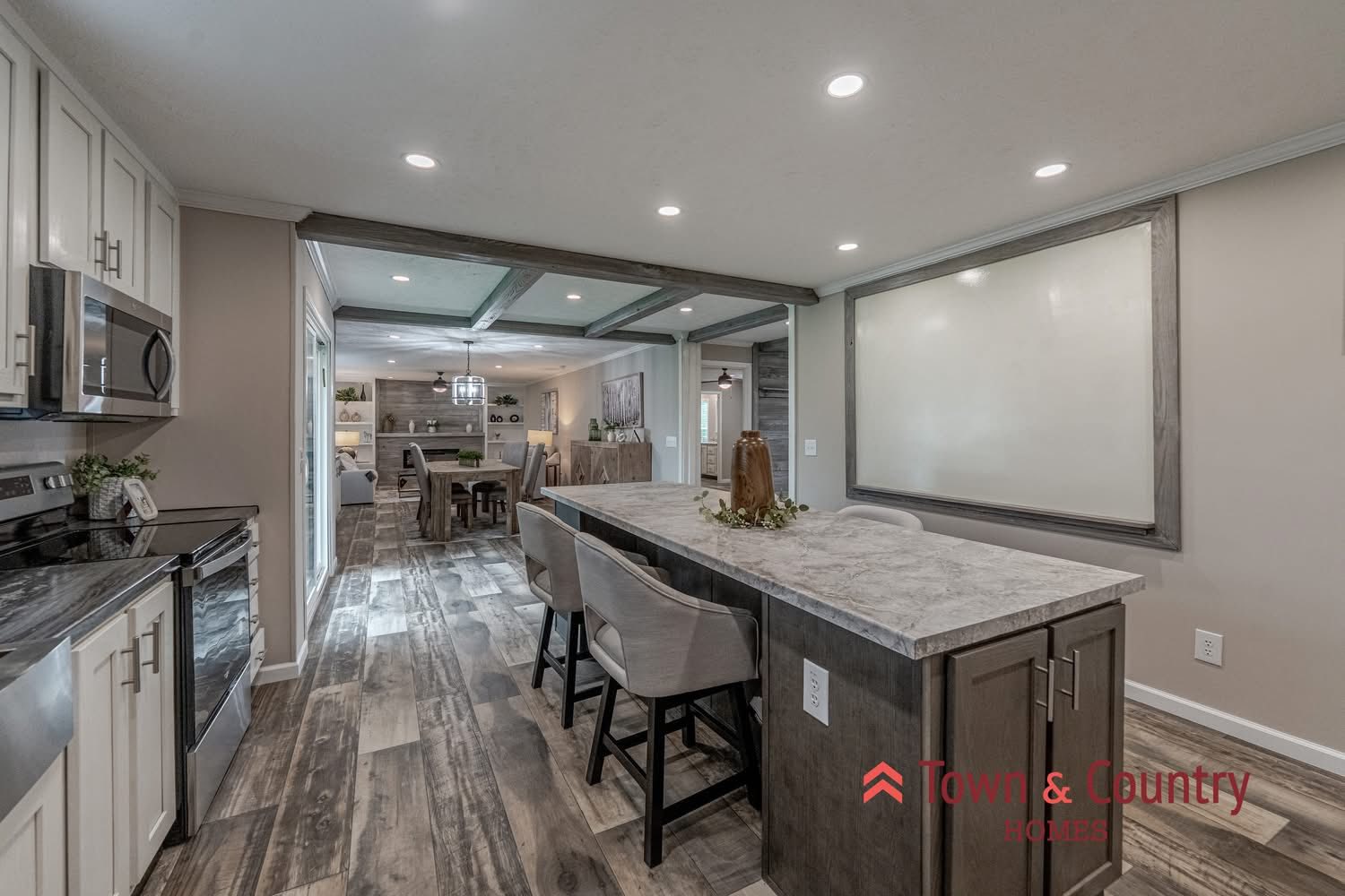Modern kitchen and dining area with recessed lighting, featuring a long island with three upholstered stools. The space has wood flooring and white cabinets, creating a warm, inviting atmosphere.