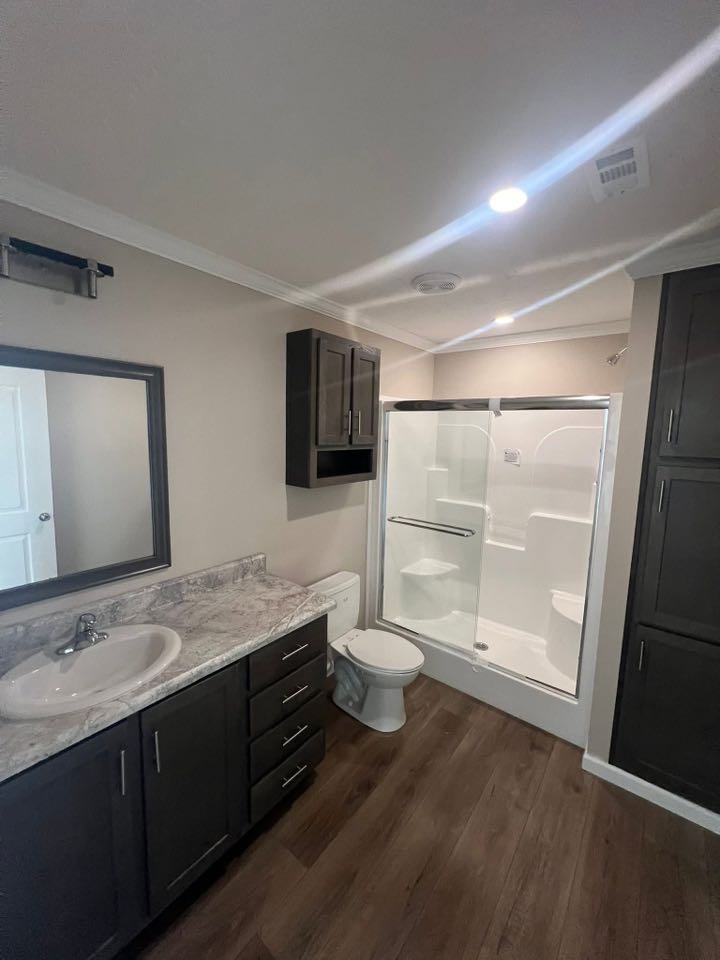 Modern bathroom with dark wood cabinets, marble countertop, and sink on the left. A glass-enclosed shower with a sliding door is next to the toilet.