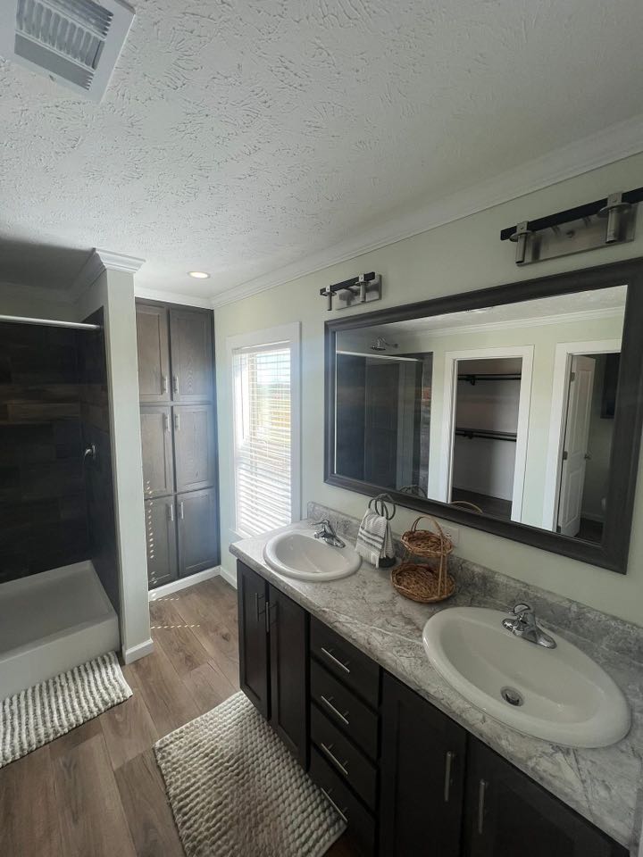 Modern bathroom with dual sinks set in a marble countertop, large mirror, dark wood cabinets, and a shower. Natural light from a window creates an inviting atmosphere.