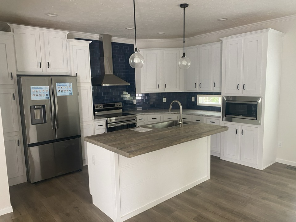 Modern kitchen with white cabinets and dark wood floors. Features a stainless steel fridge and stove, blue tile backsplash, and pendant lights.
