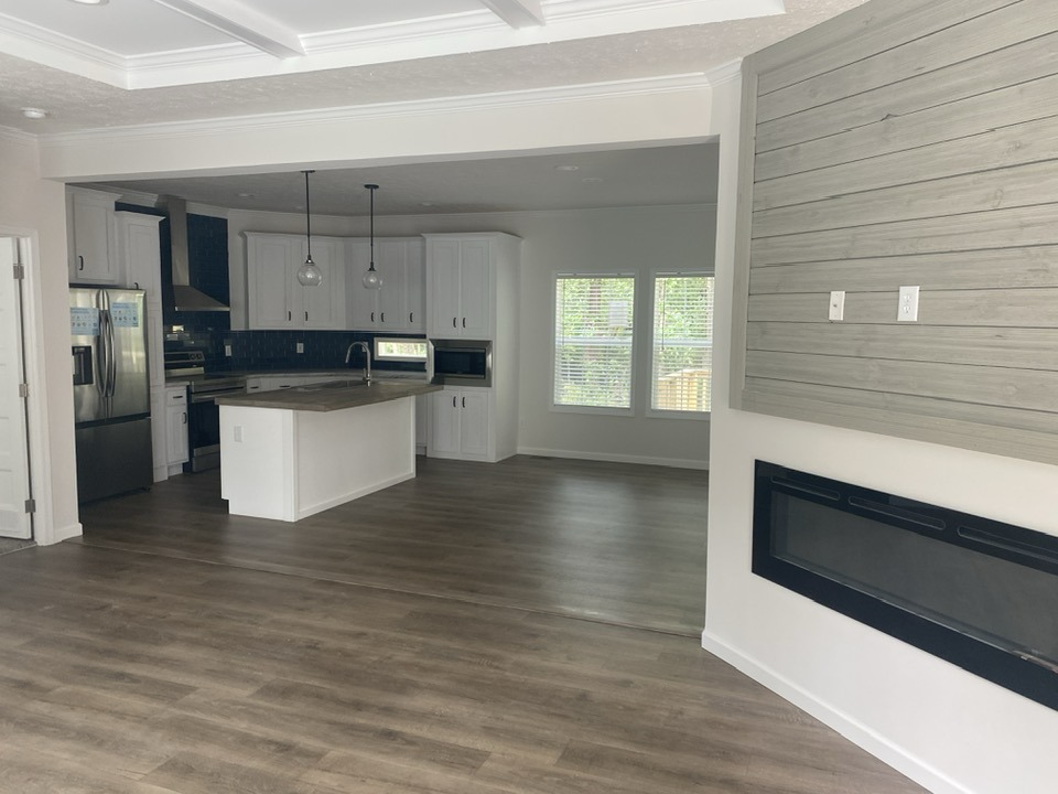 Spacious, modern kitchen with white cabinets, a central island, and stainless steel appliances. Wooden floors and large windows. Cozy atmosphere.