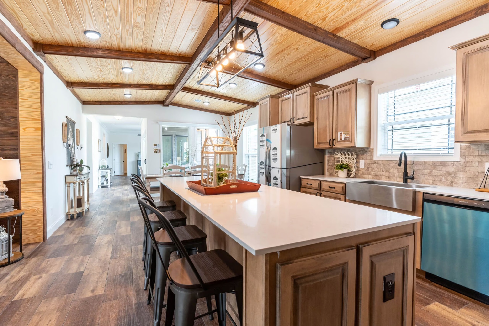 Spacious kitchen with wood ceiling beams, an island with stools, pendant lights, and stainless steel appliances. Bright, inviting, and modern.