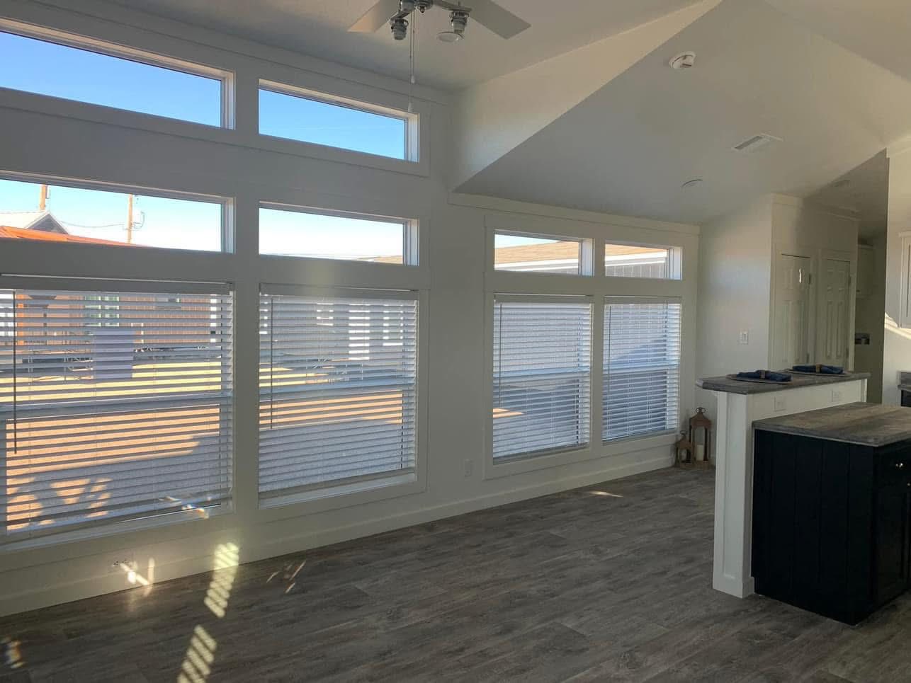 Bright, airy room with large windows letting in light. White walls, wooden floor, and modern minimal decor give an open and fresh feel.