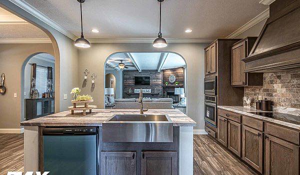 Spacious kitchen with wooden cabinets and island features stainless steel appliances. Pendant lights hang above, leading into a cozy living room.