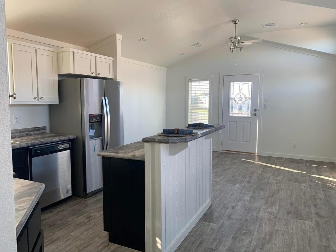 Bright kitchen with white cabinets, stainless steel appliances, and a marble countertop island. Sunlight streams through a glass-paneled door.