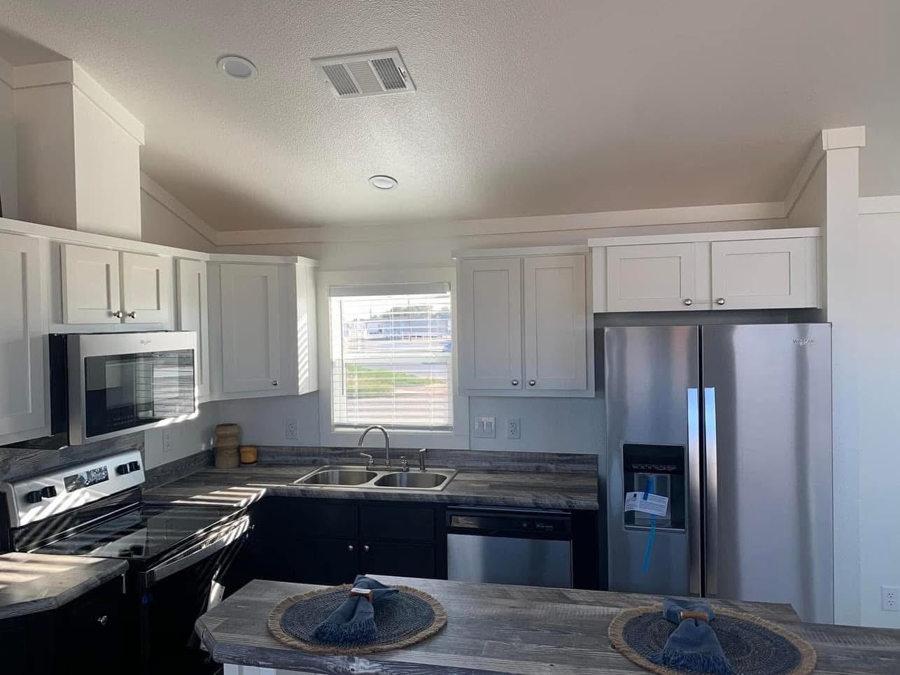 A modern kitchen with stainless steel appliances, white cabinets, and a gray countertop. Sunlight streams through a window, creating a warm, inviting atmosphere.