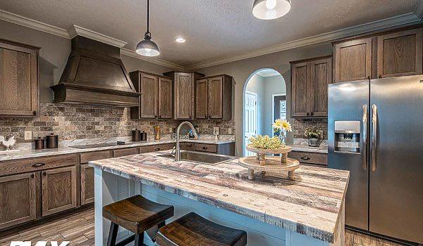 Spacious rustic kitchen with wooden cabinets, a farmhouse island with stools, and stainless steel appliances. Warm lighting creates a cozy atmosphere.