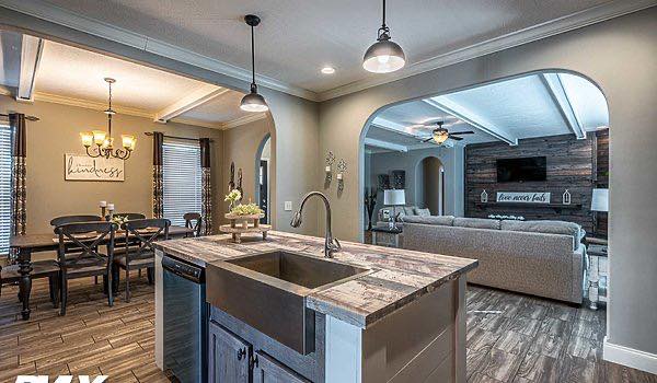 Open-plan kitchen and living area with rustic decor. Features a farmhouse sink, island, dining table, neutral tones, and a cozy living room. Warm and inviting.