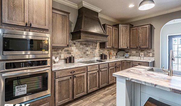 Warm kitchen with wooden cabinets and floors, stone backsplash, stainless steel appliances, and a central island. Inviting and stylish atmosphere.