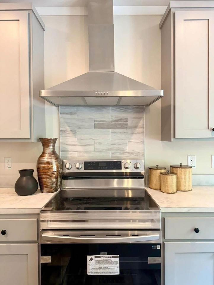 Modern kitchen with a sleek stainless steel stove and range hood, flanked by gray cabinets. Decorative vases and jars add a cozy accent.
