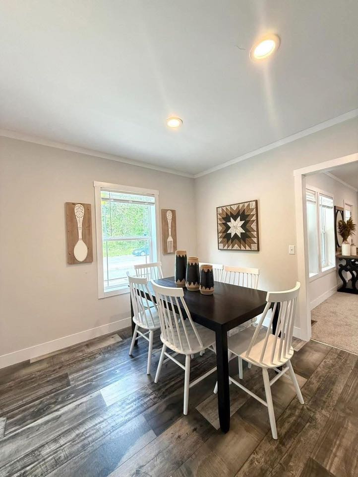 A cozy dining area with a dark wooden table, six white chairs, and decorative black vases. Wall art includes a geometric star and wooden spoon designs.