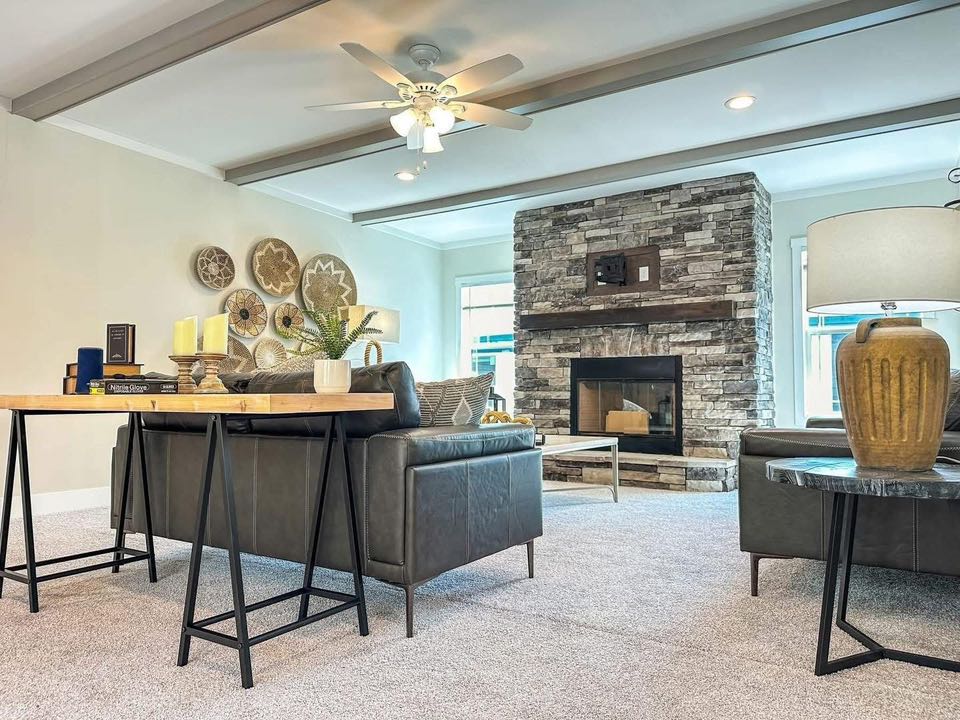 Spacious living room with modern decor; features a stone fireplace, black leather sofas, a wood-beamed ceiling, wall art, and soft lighting, creating a cozy ambiance.