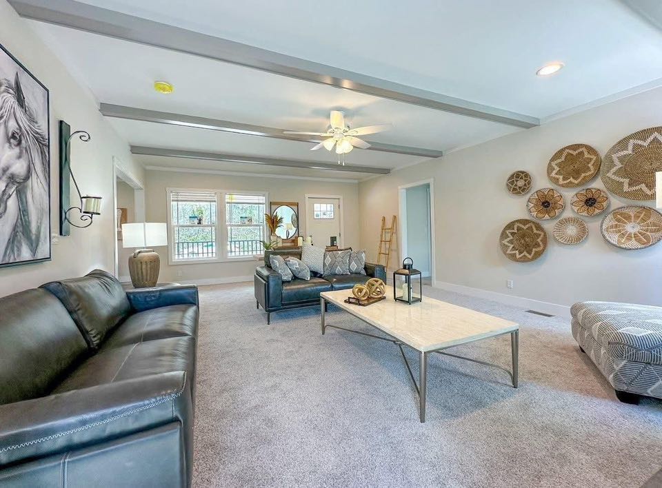 Spacious living room with a modern aesthetic featuring a black leather sofa, gray loveseat, large marble coffee table, and woven wall art. Bright, airy vibe.