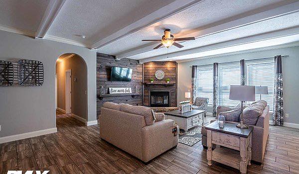 Cozy living room with beige sofas, a wooden coffee table, and a fireplace. Ceiling fan above, large window with curtains to the right, and TV on the wall.