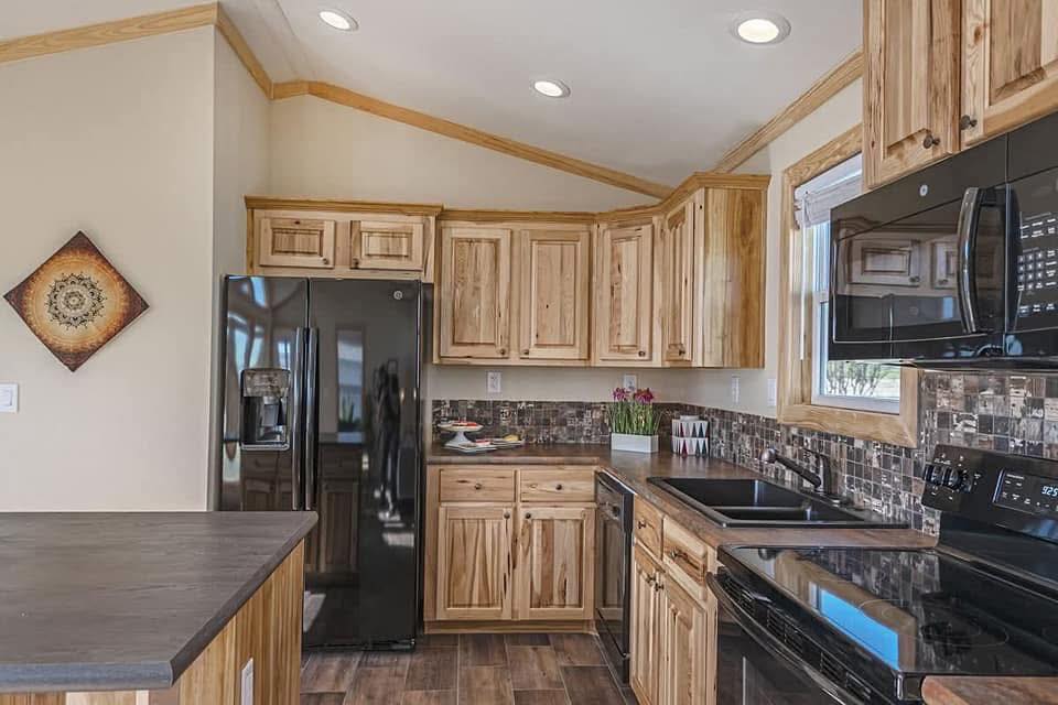 Rustic kitchen with wooden cabinets, dark countertops, and black appliances. A decorative round art piece hangs on the wall, creating a cozy atmosphere.