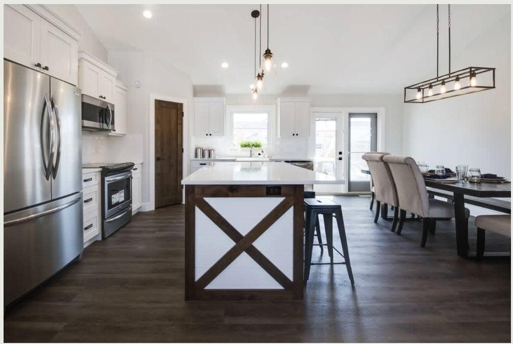 Modern kitchen with a central island featuring a wooden X design, stainless steel appliances, white cabinets, and a dining area with cushioned chairs. Bright, airy feel.