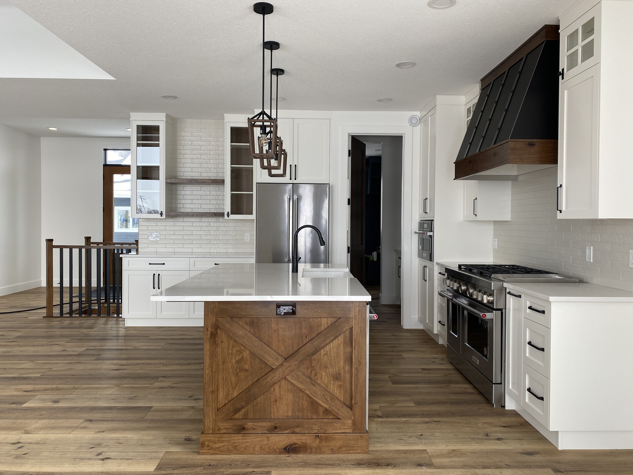 Modern kitchen with white cabinets, stainless steel appliances, and a large island featuring a wooden base and sleek countertops. Light wood floors add warmth.