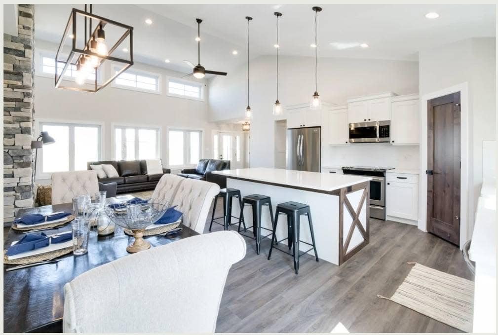 A modern, open-concept kitchen and living area with high ceilings. Features white cabinets, a large island with bar stools, and dining table set with blue napkins.