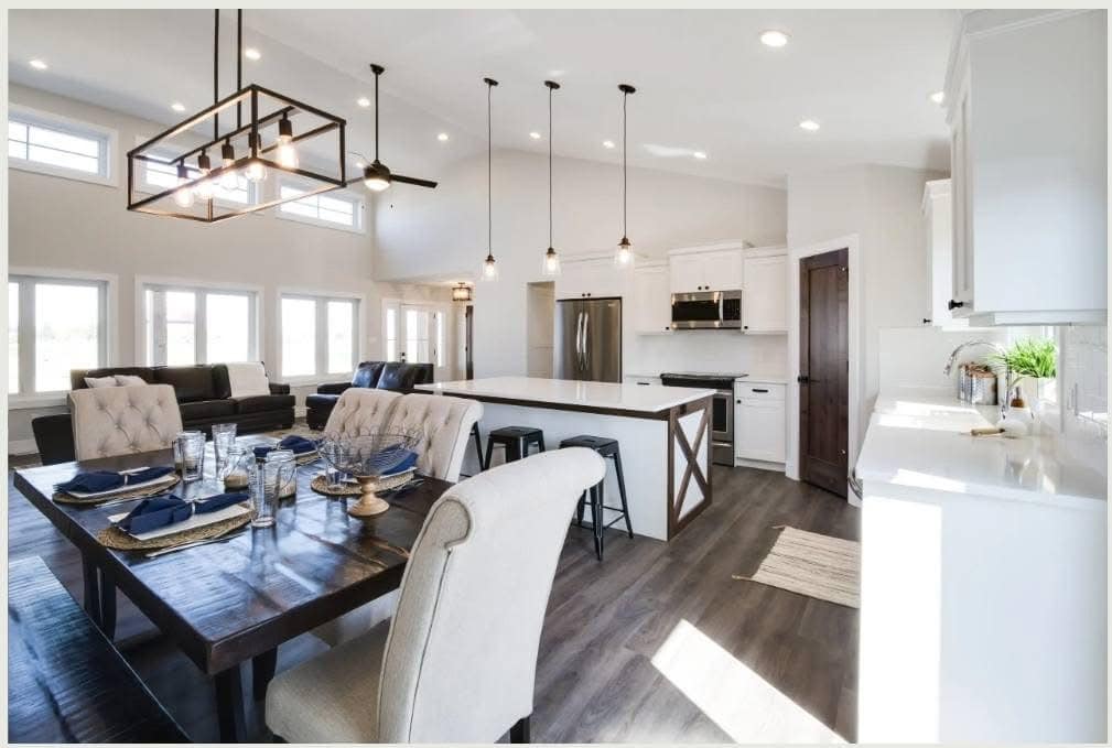 Modern open-concept kitchen and dining area with high ceilings, white cabinets, large island, pendant lights, dark dining table, and upholstered chairs.