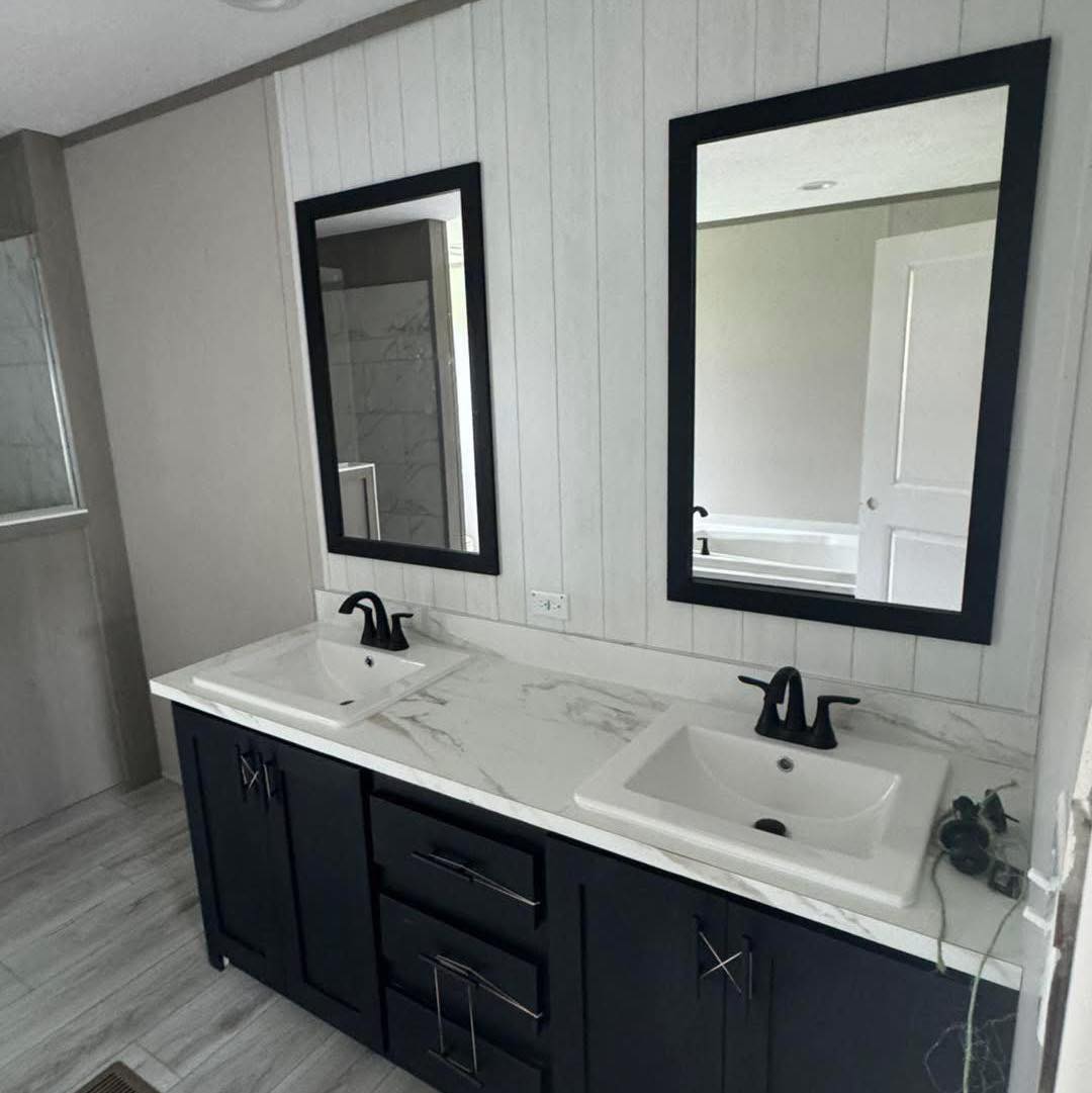 A modern bathroom features a dual-sink vanity with a marble countertop, black faucets, and sleek black-framed mirrors on a paneled wall. Soft lighting creates a clean, sophisticated atmosphere.