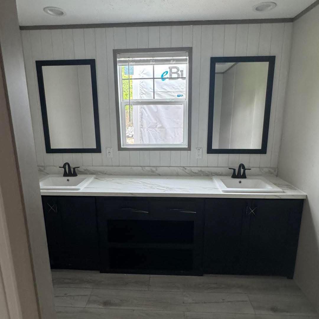Modern bathroom with dual sinks on a white marble counter, two black-framed mirrors, black faucets, a white paneled wall, and a central window.