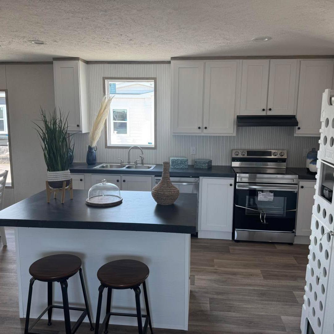 Modern kitchen with white cabinets, black countertops, and stainless steel appliances. Features a central island with two stools and decor items, exuding a stylish and cozy ambiance.