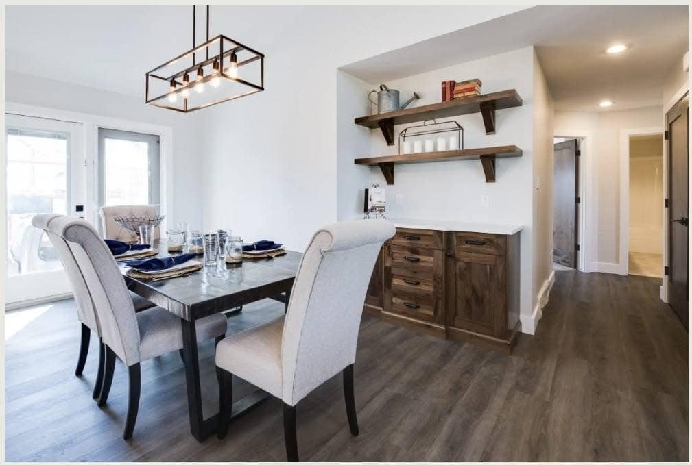 A modern dining room with a gray marble table, beige upholstered chairs, and minimalist decor. Wooden shelves and cabinets add warmth, while large windows bring in natural light. The room feels contemporary and inviting.