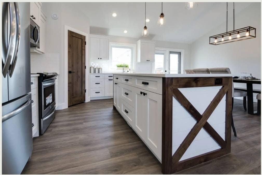 Modern kitchen with white cabinets and wood accents. Central island features X-shaped design. Stainless steel appliances and pendant lights add elegance.