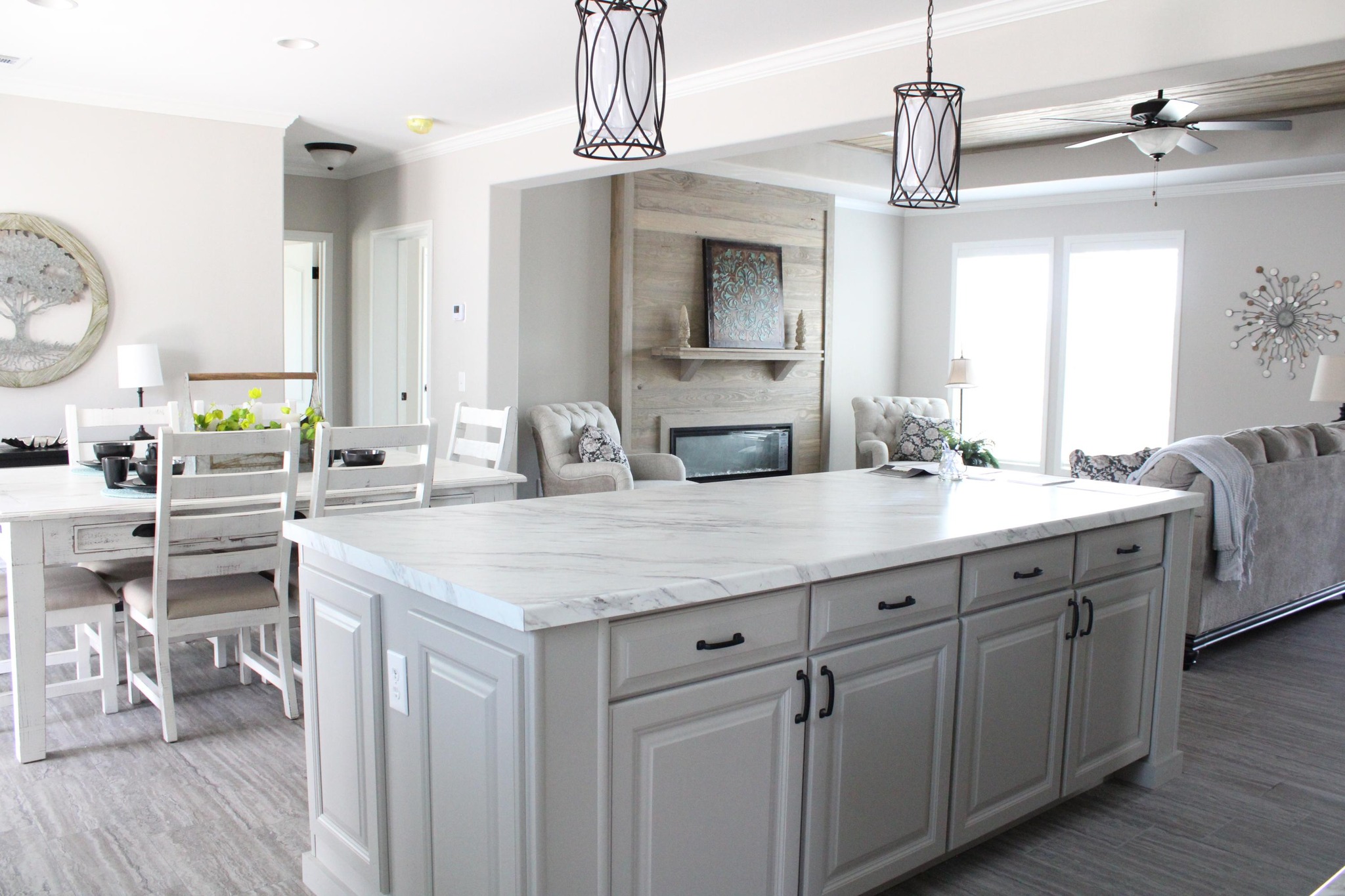 A modern kitchen and living area featuring a marble island, white cabinetry, elegant pendant lights, a dining table, fireplace, and cozy seating. Bright and airy.
