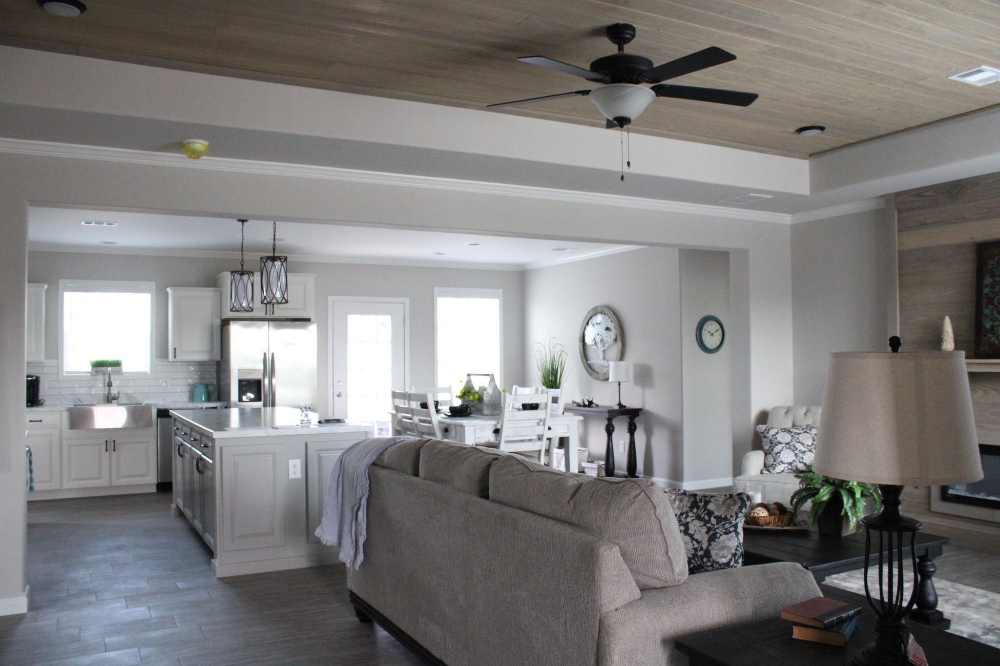 Modern open-concept living area with elegant kitchen, large beige sofa, dark wood coffee table, ceiling fan, and soft natural lighting. Cozy and inviting.
