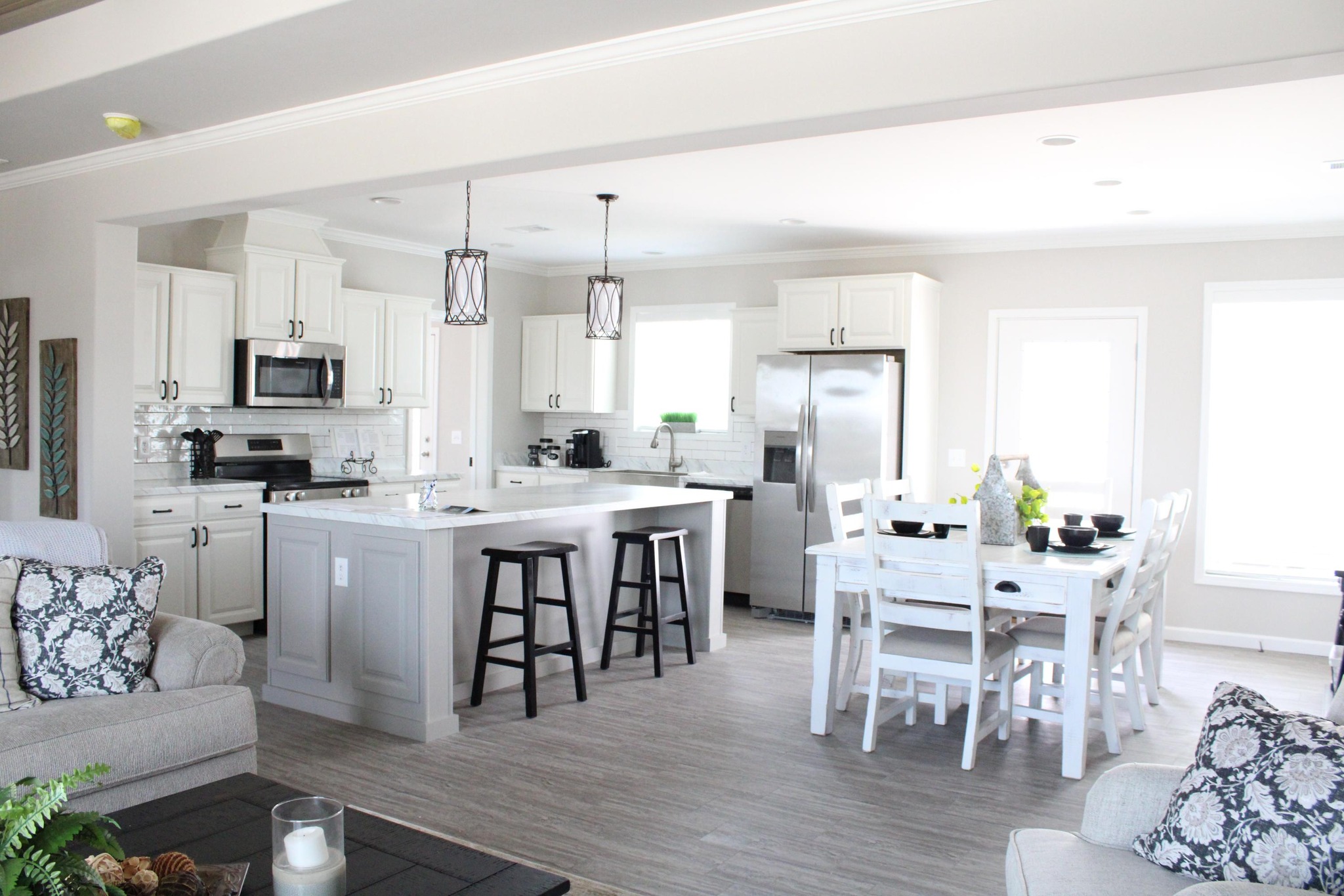 Bright, modern kitchen with white cabinets and a large island with dark stools. Adjacent dining area with white table, chairs, and decorative accents.