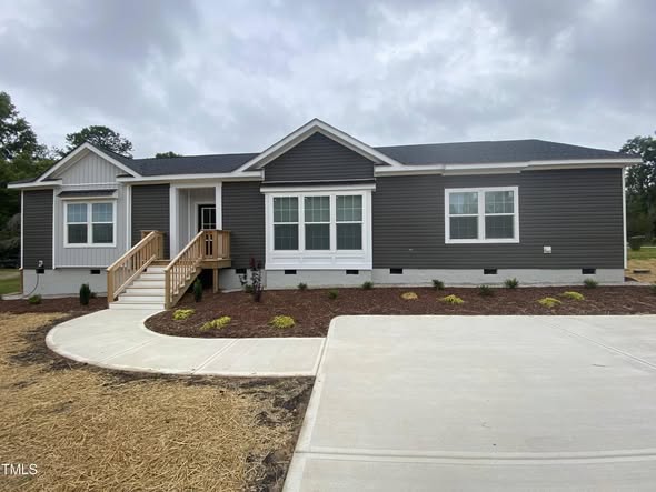 Single-story gray house with white trim, large windows, a small wooden porch, surrounded by a neat garden, and set against a cloudy sky.
