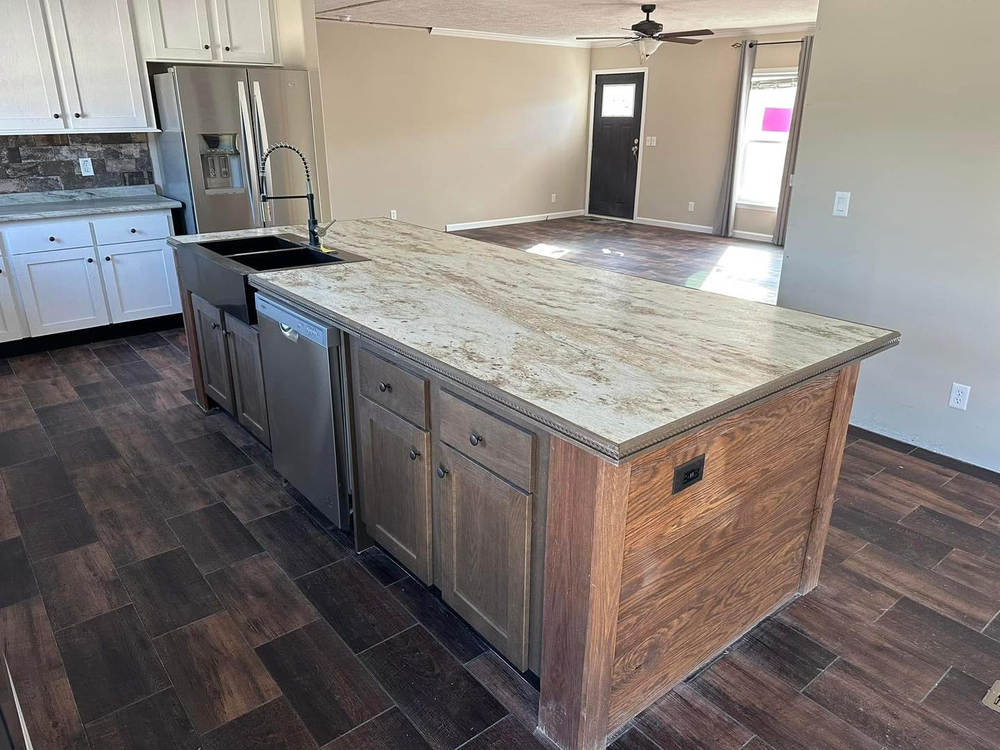 Spacious kitchen with a large island featuring a marbled countertop and wood cabinets. Stainless steel appliances and dark wood flooring add a modern touch.