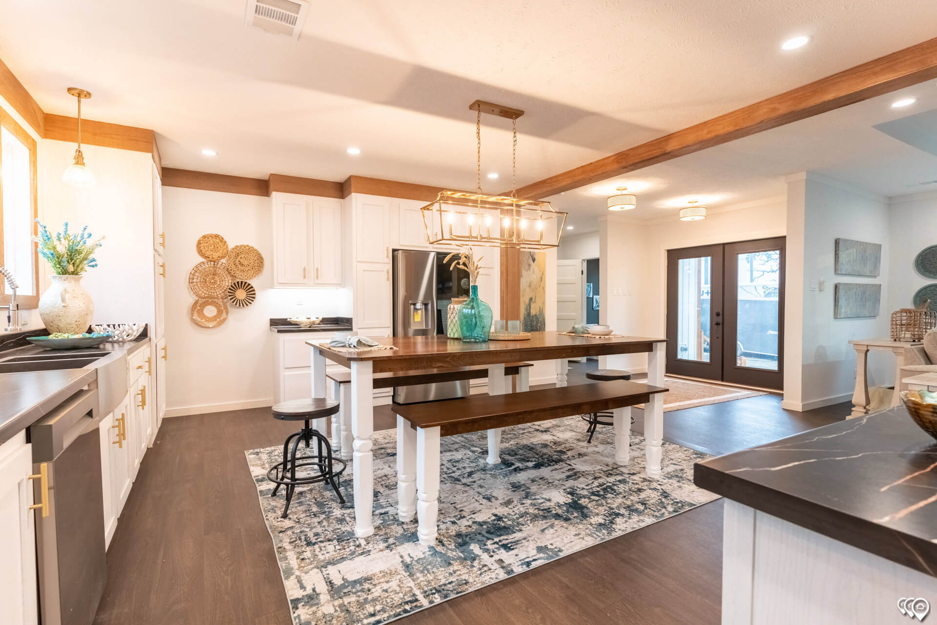 Bright, cozy kitchen with a large wooden island, pendant lighting, and a decorative centerpiece. White cabinetry, stainless steel fridge, and woven wall decor.