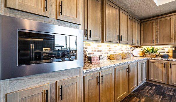 Bright living space with dark wooden floors and ceiling beams. A modern, open kitchen with a dining area, geometric rug, and large windows create a warm, inviting atmosphere.