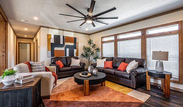 Modern living room with dark leather sofas, colorful cushions, large abstract wall art, and a geometric rug. Bright natural light from wide windows.
