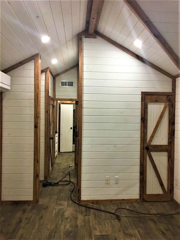 Cozy interior hallway with white shiplap walls and wooden accents. Doors with diagonal wood patterns. Warm lighting creates an inviting rustic feel.