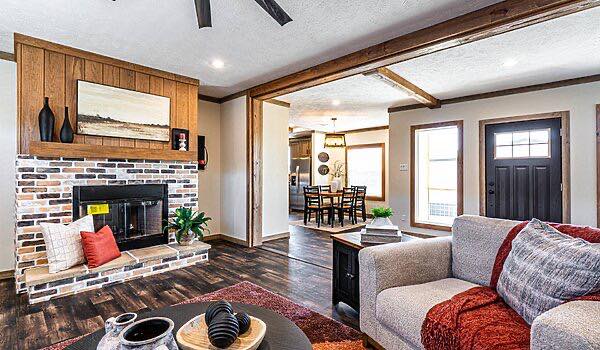A cozy living room features a brick fireplace with modern decor, adjacent to a dining area. Warm tones and natural light create an inviting atmosphere.