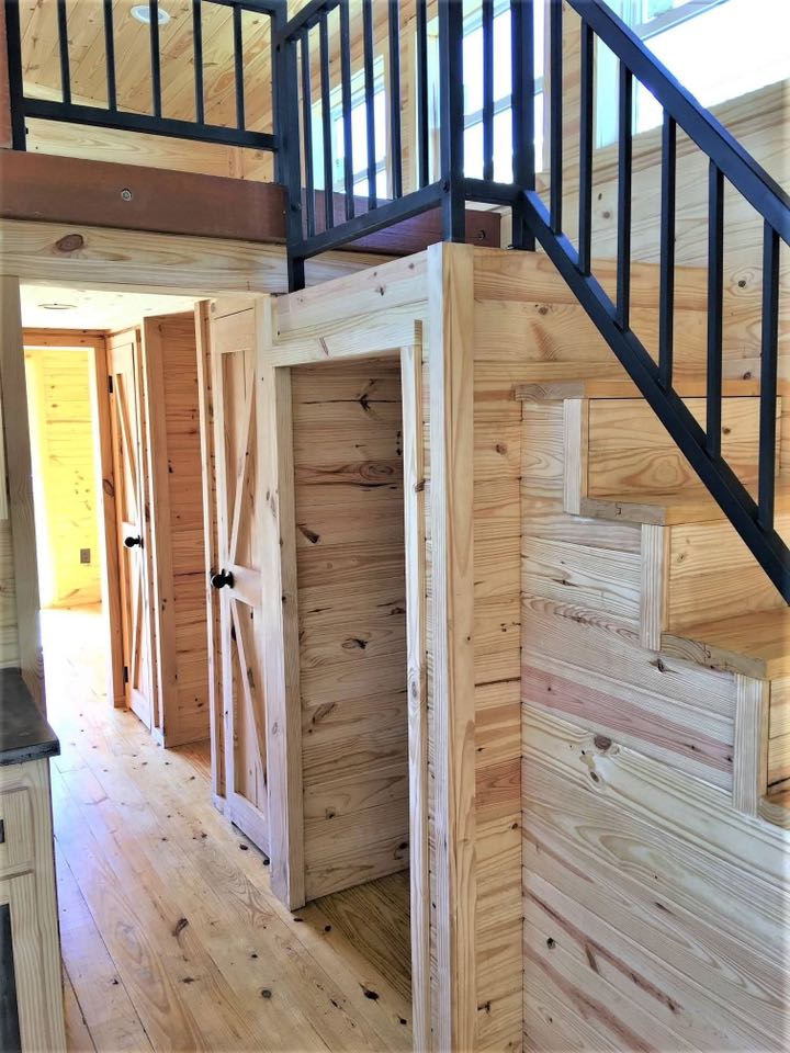 Wooden interior of a compact living space featuring natural pine walls and floor, black metal staircase, and rustic barn doors. Bright and cozy atmosphere.