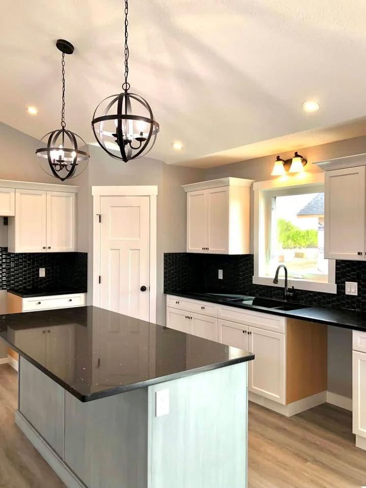 Modern kitchen with white cabinets, black countertops, and an island. The room is lit by globe-shaped pendant lights, creating a sleek and inviting atmosphere.